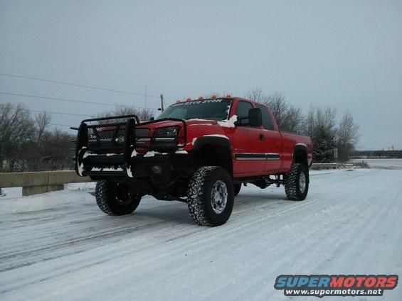Red pickup truck with a large bull bar and lifted suspension on a snowy road