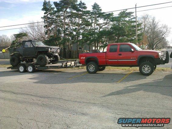 Modified black SUV on trailer towed by red pickup truck