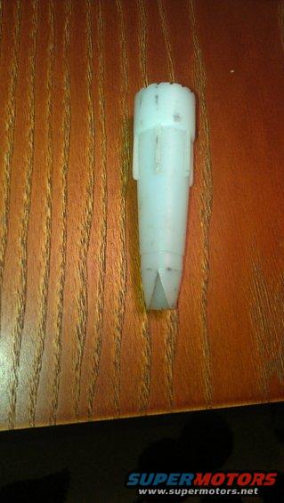White plastic automotive part with a tapered end, resting on a wood-grain surface