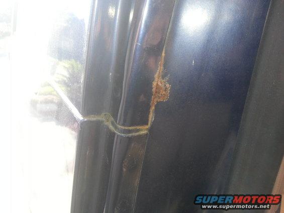 Close-up of rust forming on the door frame of a dark-colored vehicle