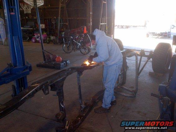 Man welding a vehicle frame in a garage with a lift and bicycles