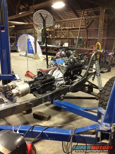 Jeep frame on lift with engine and transmission installed, in a garage with a basketball hoop