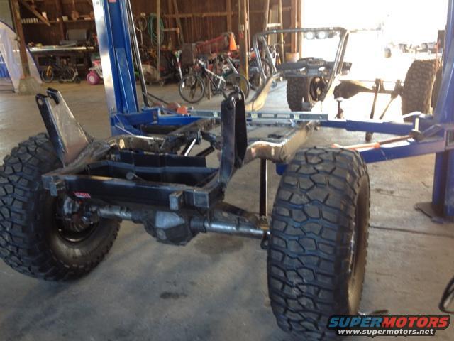 Jeep CJ frame with large tires, lifted on a blue car lift inside a garage
