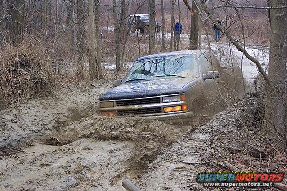 Muddy SUV stuck in a ditch with another vehicle and people in the background