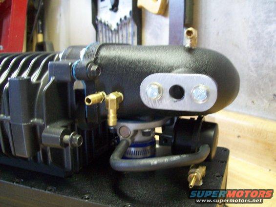 Black supercharger with brass fittings and a metal plate with two holes