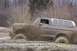 1978 Ford Bronco - A 1978 Ford Bronco navigates a challenging muddy off-road course, kicking up significant spray.