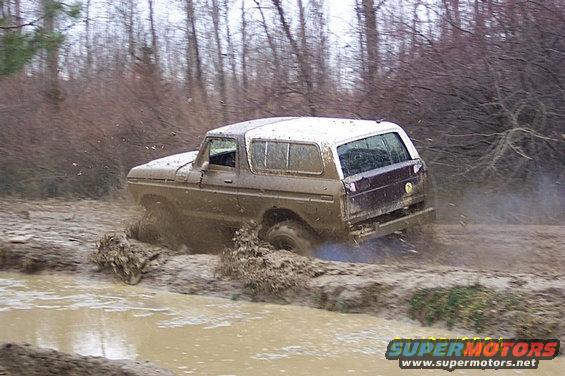1978 Ford Bronco navigating a muddy trail, kicking up spray