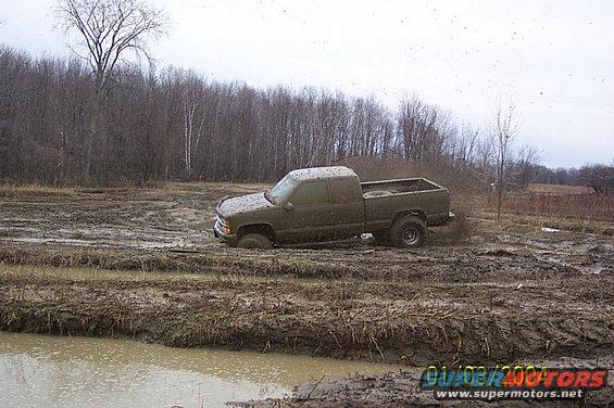 Pickup truck stuck in a muddy field with trees in the background
