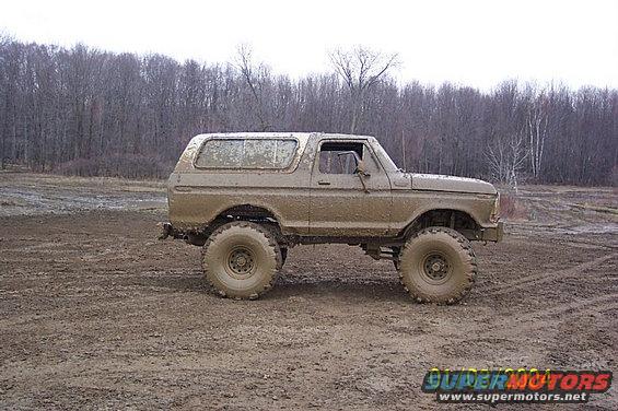 Mud-covered 1978 Ford Bronco parked on a muddy field with trees in the background