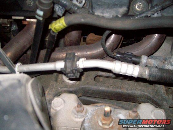 Close-up of engine components including exhaust manifold and AC line