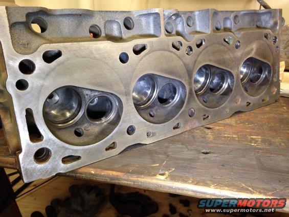 Engine cylinder head with valves visible, resting on a wooden surface