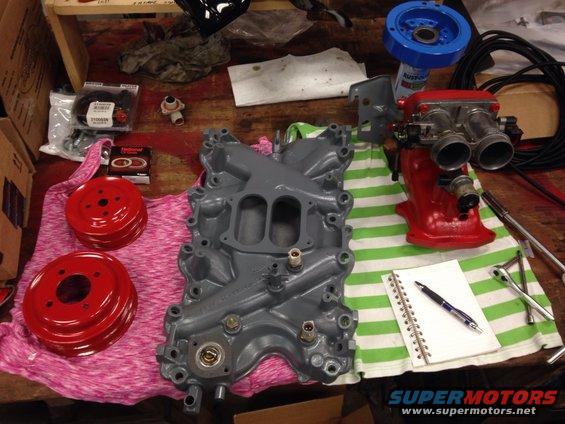 Gray intake manifold and red throttle body with pulleys and a notebook on a workbench