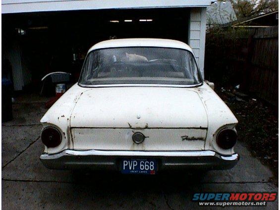 Rear view of a white 1960 Ford Falcon parked in front of a garage. It has a license plate that reads PVP 668