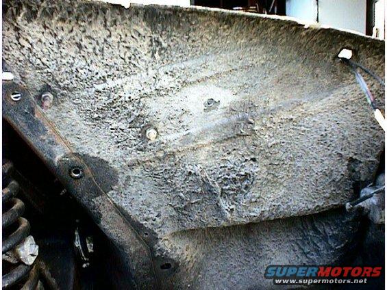 Undercarriage of a vehicle with heavy rust and dirt buildup, showing suspension components and frame