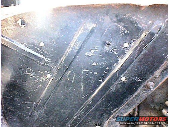 Scratched black metal underbody panel with visible fasteners and some faint markings