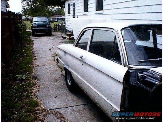 1960 Ford Falcon sedan, white, undergoing repairs. Another dark SUV parked in background