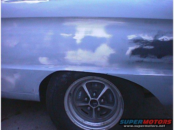 Close-up of a car's side panel and wheel, showing reflections of clouds