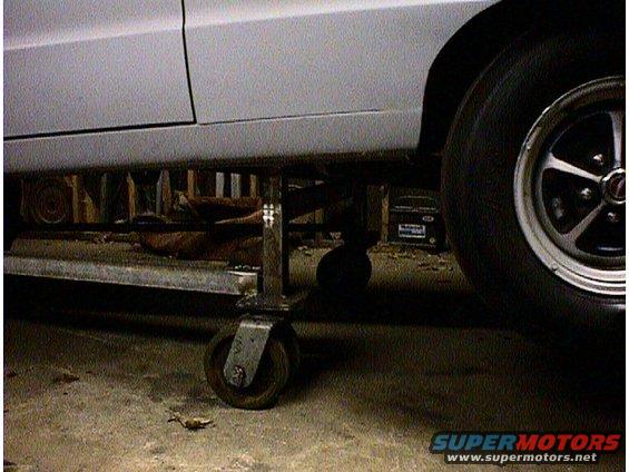 White car body on metal jack stands, close-up on side panel and wheel