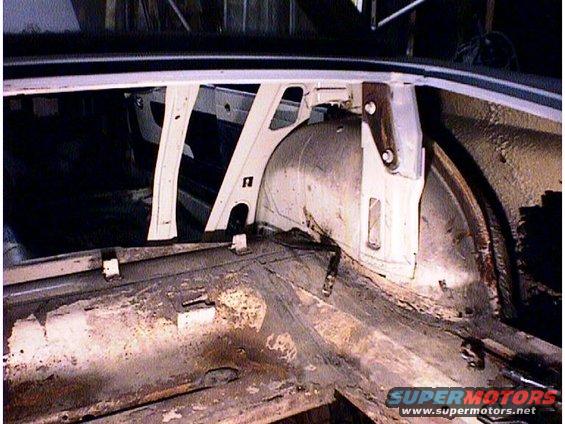 Interior view of a car's rear wheel well area, showing rust and structural components