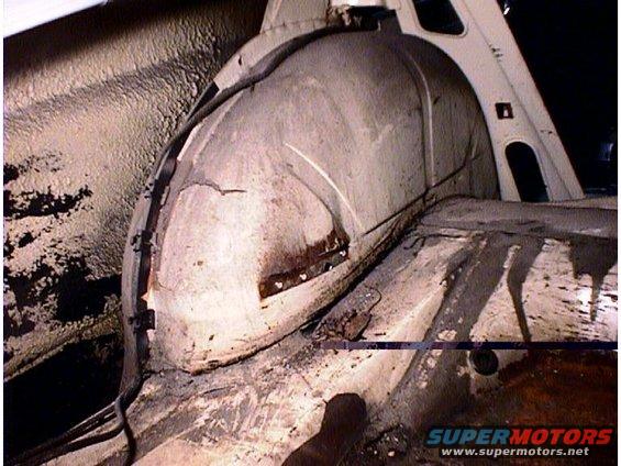 Inside of a car's rear wheel well and floor pan, showing some rust and dirt