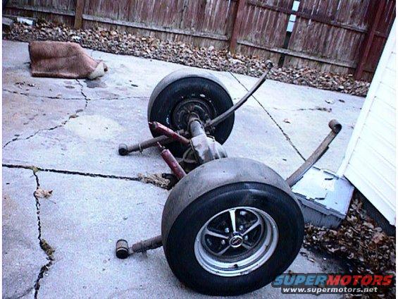 Rear axle assembly with two wheels and leaf springs, sitting on a cracked concrete surface