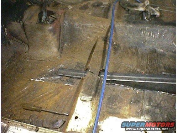Rusty car floor with a screwdriver and a blue wire