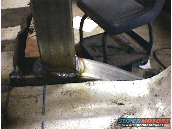 Close-up of a welded metal joint on a vehicle frame, with a black seat visible in the background