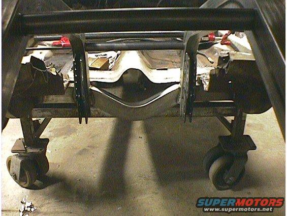 Car frame on casters, viewed from the rear. The chassis is exposed with suspension components visible