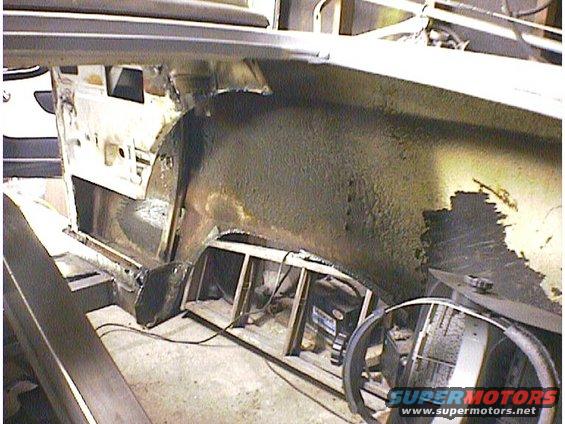 Car interior showing rusted wheel well and floor pan, with visible steering wheel and SuperMotors logo