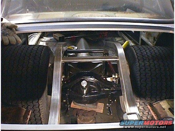 Car trunk interior showing rear axle, suspension, and tires. Metal framing is visible