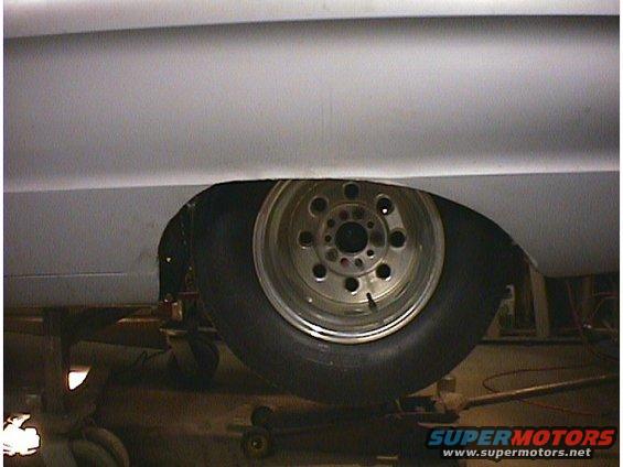 Car's rear wheel well with a drag slick tire and a polished aluminum wheel. The car is on jack stands