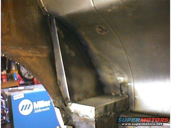 Close-up of welded metal frame components inside a vehicle, with a blue Miller welding machine visible