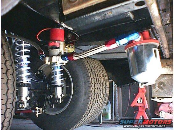 Underbody view of a Holley fuel pump and filter with braided lines, next to a tire and suspension components