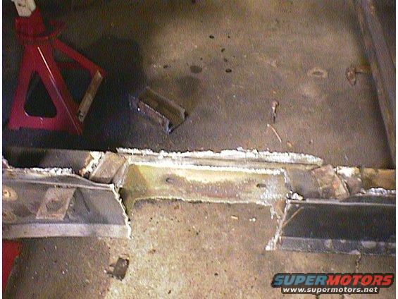 damaged car frame with a red jack stand nearby