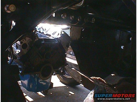 Car engine bay with engine partially visible, some frame components and a tire