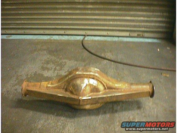 Rusty rear axle housing on a concrete floor in front of a ribbed metal door