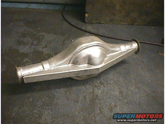 Aluminum rear axle housing with visible welds, resting on a dark floor