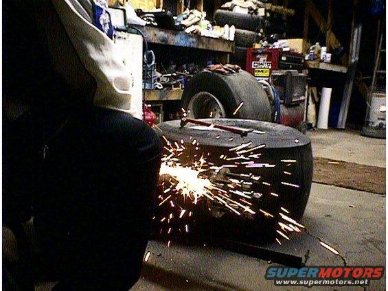 Person in protective gear welding sparks flying off a large tire in a workshop