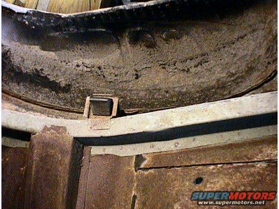 Close-up of rusted metal frame and undercarriage components with a small black bracket attached
