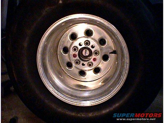Close-up of a shiny aluminum wheel with multiple lug nut holes, mounted on a black tire