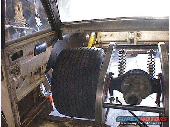 Rear axle assembly with dual coil springs and a large tire mounted inside a vehicle's chassis