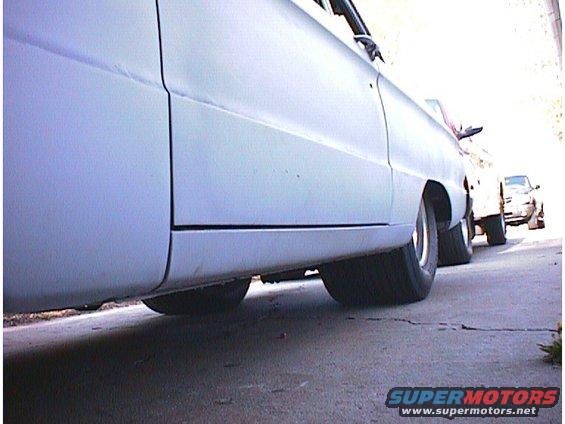 Light blue car side view, showing rear wheel and part of the door seam. Other cars are visible behind it