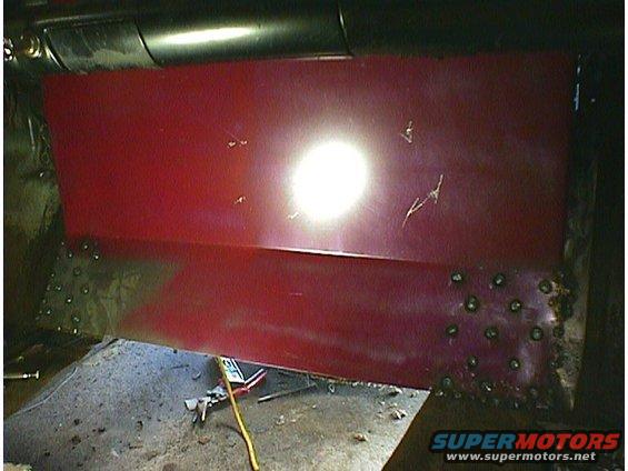 Red car door panel with visible weld marks and scratches. A bright light reflects off the surface