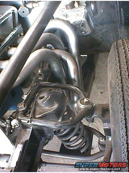 Close-up of custom exhaust headers and front suspension components, including a coil spring and control arm