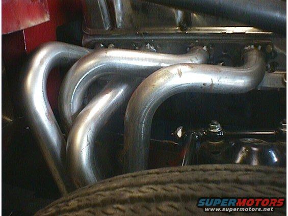 Close-up of shiny metal exhaust pipes on an engine, with a tire visible in the foreground
