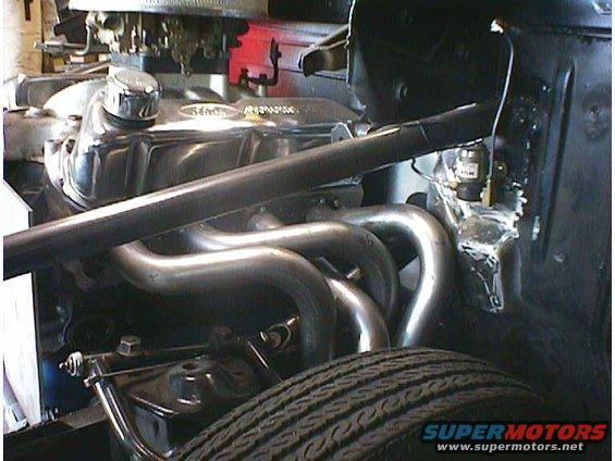 Close-up of a V8 engine with chrome valve covers and custom exhaust headers, tire in foreground