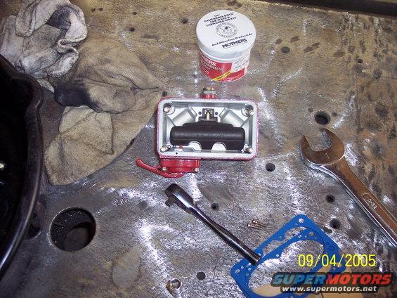 Brake master cylinder parts on a metal workbench with a wrench and a can of Mothers polish