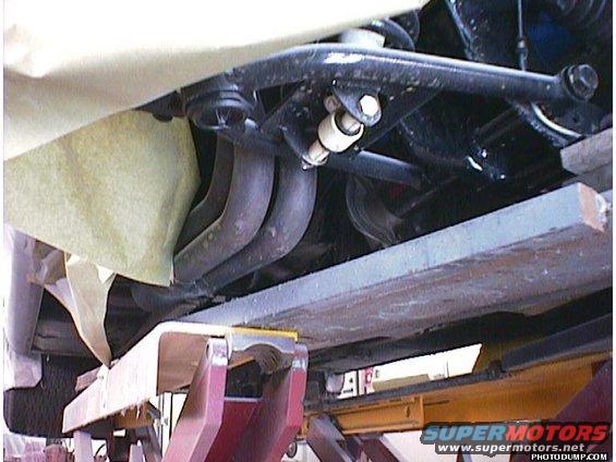 Undercarriage of a vehicle on a lift, showing exhaust pipes and suspension components