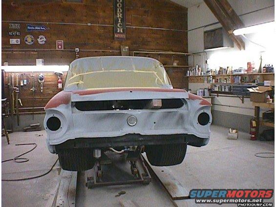 Rear view of a 1960 Ford Falcon being worked on in a garage. It's on a lift with primer on the body