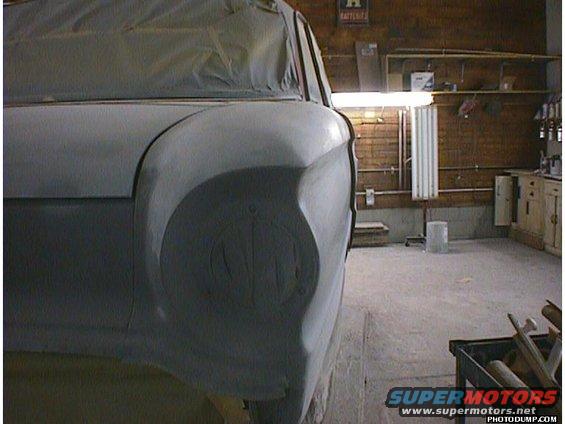 Car body in primer, front fender and headlight area visible, taped for paint